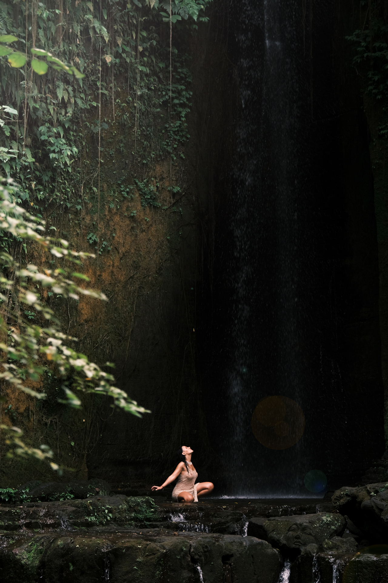 Nicole seated on sunlit rocks beside a quiet stream